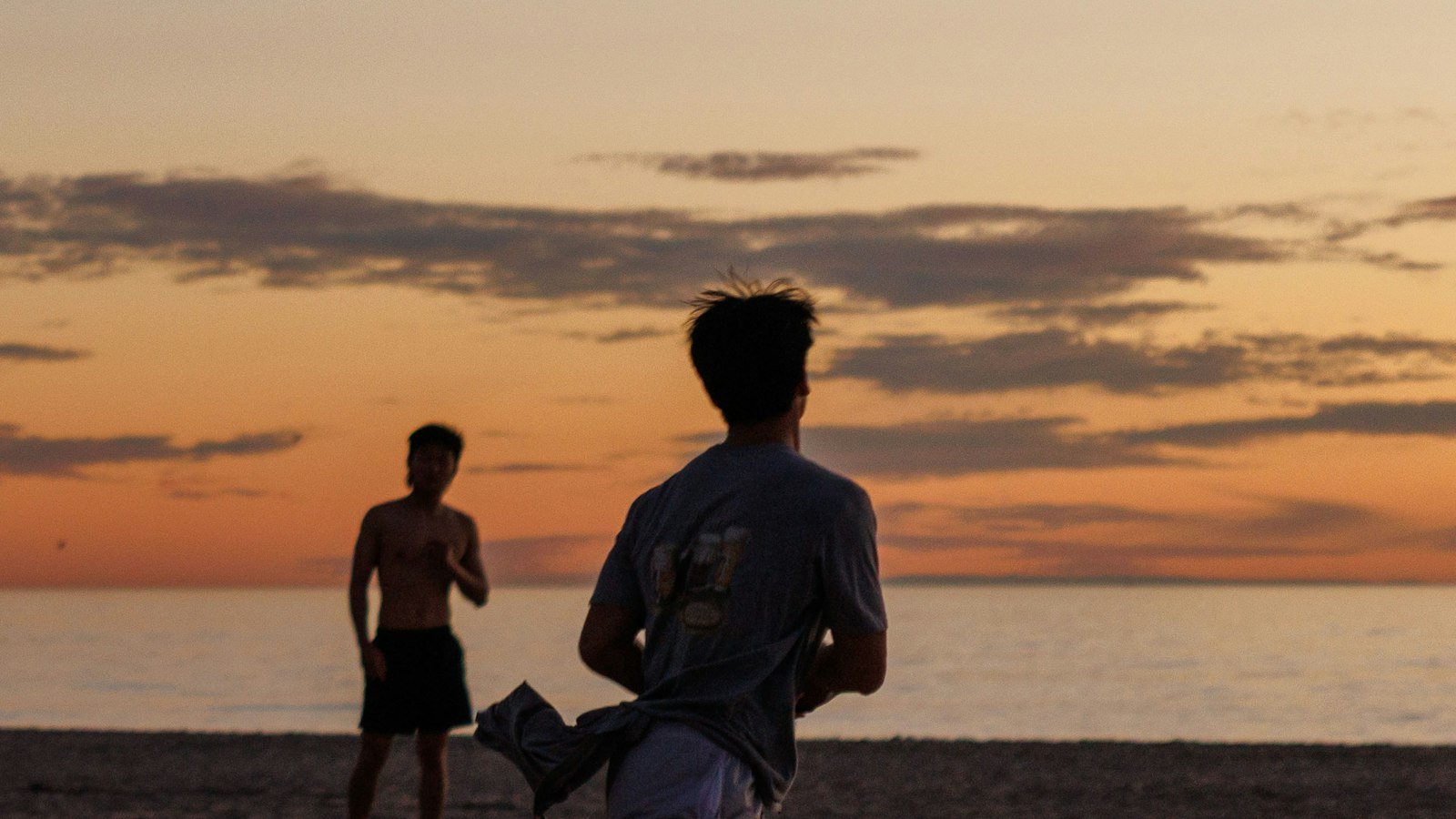Dois amigos jogando na praia ao pôr do sol