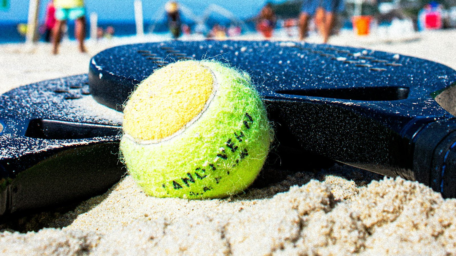 Bola sobre raquete de beach tênis na areia, com a rede ao fundo
