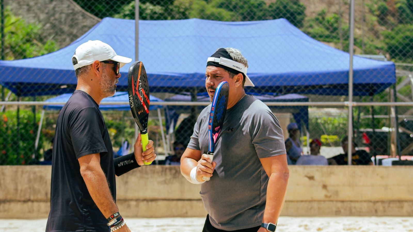 Dois jogadores de beach tênis conversam segurando as raquetes na quadra de areia